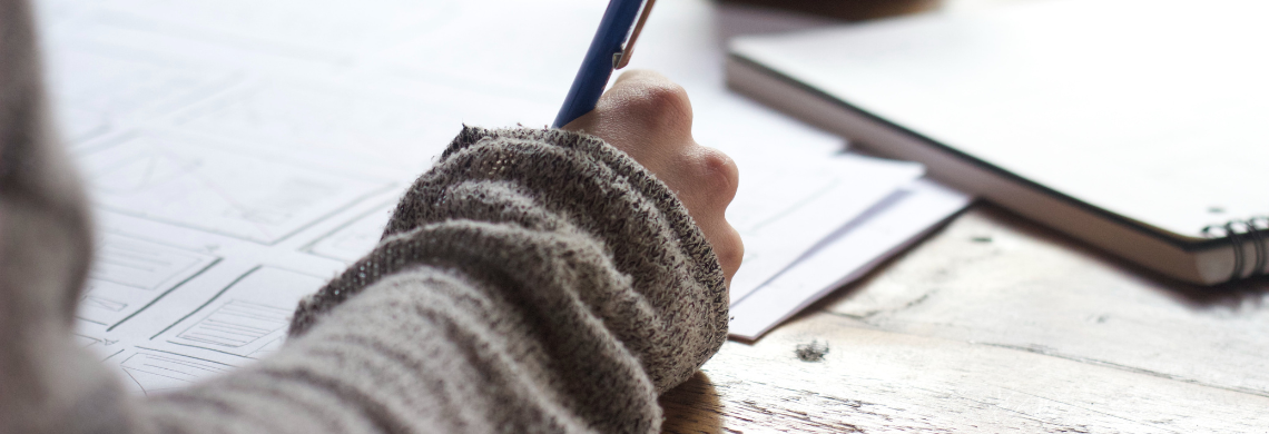 Person, die einen Stift h&auml;lt und auf ein Blatt Papier schreibt.